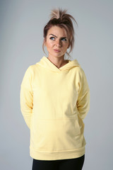 Obraz premium Close up of young attractive caucasian woman in yellow hoodies looking at camera posing funny, shocked with expression. Positive emotions of girl. Model tests on white background