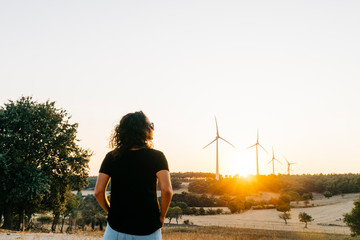 A female model who is wearing black basic t-shirt and at back ground renewable energy wind turbines...