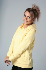 Close up of young attractive caucasian woman in yellow hoodies looking at camera posing funny, shocked with expression. Positive emotions of girl. Model tests on white background