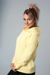 Close up of young attractive caucasian woman in yellow hoodies looking at camera posing funny, shocked with expression. Positive emotions of girl. Model tests on white background