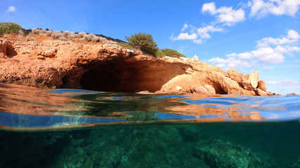 Above and below underwater photo of tropical exotic island arch cave with emerald sea and deep blue...
