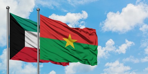 Kuwait and Burkina Faso flag waving in the wind against white cloudy blue sky together. Diplomacy...