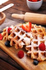 Traditional belgian waffles with fresh blueberries, sugar and raspberries on rustic table