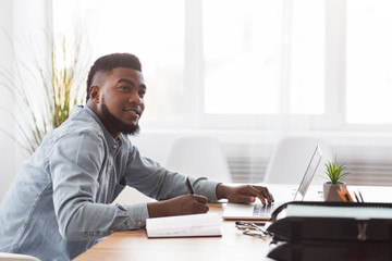 Black man taking notes from laptop at workplace in office