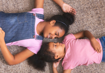 Loving african american sisters lying together on floor