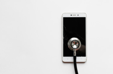 Closeup of black stethoscope on broken mobile smartphone after drop, view from above, on white background. Copy space. Smart phone with cracked screen or touchscreen and damaged case.