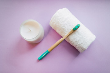 Fototapeta na wymiar Bamboo toothbrush on pink background with white towel and a candle. Eco friendly concept. Top view.