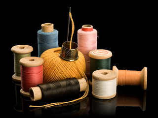 Group of old coils with multi-colored threads and needle with thimble from brass - obrazy, fototapety, plakaty