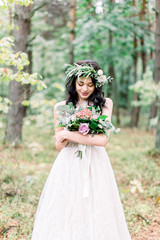 Obraz na płótnie Canvas beautiful bride in nature in a coniferous forest in a wreath on her head and a luxurious wedding dress. Rustic boho style of wedding outdoors
