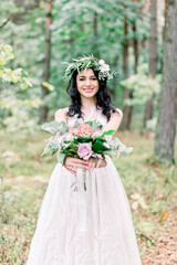 Fototapeta na wymiar Portrait of a young beautiful bride with eucalypthus wreath on the head, with a rustic bouquet in the forest at wedding walk.