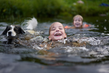 Two children and a dog swim in a river near the shore.  The mood of summer, warmth and joy from...