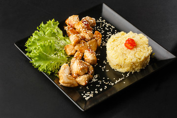 Chicken with sweet and sour sauce. Fried chicken pieces in batter with sweet and sour sauce. Chinese chicken sweet and sour sauce, served with ouscous and vegetables on dark background. Horizontal.