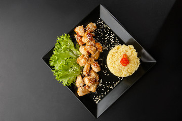 Chicken with sweet and sour sauce. Fried chicken pieces in batter with sweet and sour sauce. Chinese chicken sweet and sour sauce, served with ouscous and vegetables on dark background. Horizontal.