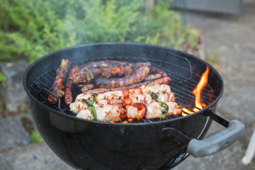 Delicious outdoor barbecue food. Close up of a black bbq grilling chicken, sausages, vegetables. Looks yummy !