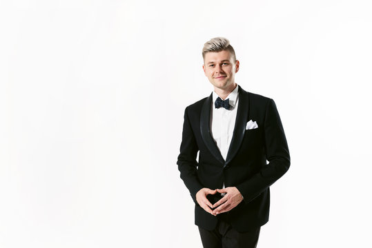 Portrait of young smiling handsome man in tuxedo stylish black suit, studio shot isolated on white background. Showman or toastmaster in jacket with bowtie