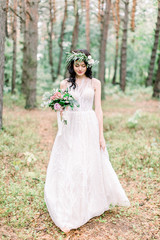 Fototapeta na wymiar Full-length view of the smiling bride in the wedding dress walking in the green forest.