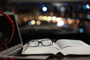 laptop with headphones and an open book with glasses, traditional reading and audiobook