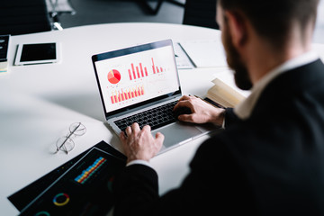 Businessman sitting in office working on statistical data of market typing on laptop in workspace in company