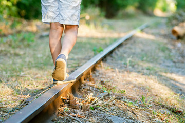 Little boy steps on the rails of the railway, being exposed to danger. Young boy balancing on a...