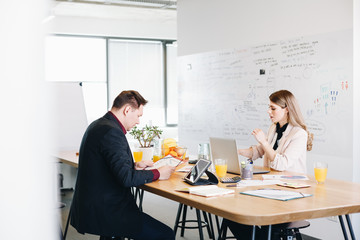 Obraz na płótnie Canvas Business woman and business man discussing new marketing strategies using graphs and laptop. Candid moment, two colleagues sitting at the table and having a meeting in the open office space..