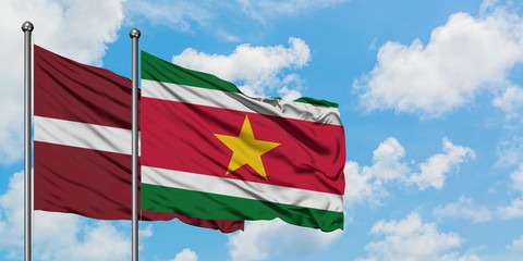 Latvia and Suriname flag waving in the wind against white cloudy blue sky together. Diplomacy concept, international relations.
