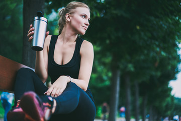 Charming good looking female runner resting on bench on urban setting after morning jogging around city, attractive sportswoman thoughtful looking away before starting hard workout on nature