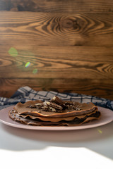 Сhocolate pancakes with chocolate and waffles on a pink plate under the sunlight in the morning and blue towel on the wooden background. Vertical