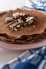 Сhocolate pancakes with chocolate and waffles on a pink plate and a cup of coffee on a white table. Vertical