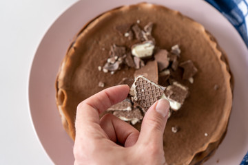 Woman holds a waffle over a white table with a plate with chocolate pancakes on it