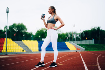 Fototapeta premium Thoughtful adult athletic female holding water bottle in stadium