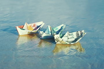 A boat made of paper money in sea sand A boat made from a dollar, euro, Russian ruble at sea. Sea...