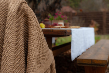 Obraz na płótnie Canvas Beige knit blanket and blurred big served table with breakfast, outdoors