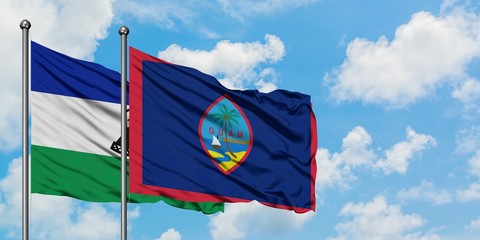 Lesotho and Guam flag waving in the wind against white cloudy blue sky together. Diplomacy concept, international relations.