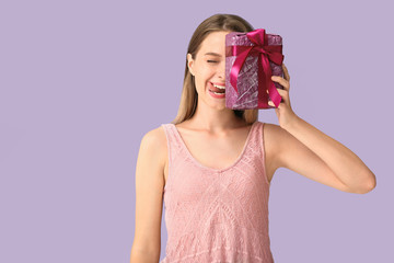 Grimacing woman with gift box on color background