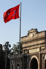 arch of the university of instanbul illuminated by the sun with a waving Turkish flag in front of it