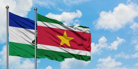 Lesotho and Suriname flag waving in the wind against white cloudy blue sky together. Diplomacy concept, international relations.