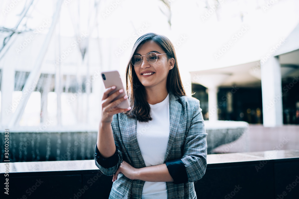 Wall mural young smiling hipster girl enjoying time for using modern technology on urban setting, happy woman c