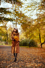 happy woman with yellow leaves walking outside in autumn park