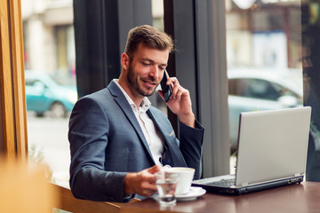 Young businessman in suit sitting in cafe bar and talking on the phone