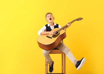 Little boy playing guitar and singing on color background