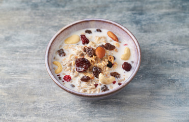 Bowl of granola with milk, nuts, raisins and cranberries. Concept for a tasty and healthy meal. Rustic wooden background. Close up.
