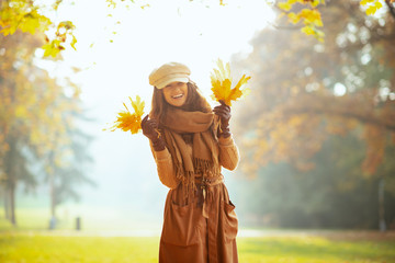 happy modern woman outside in autumn park showing yellow leaves