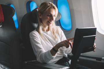 Smiling attractive female passenger searching movie to watch on board tv device during comfortable...