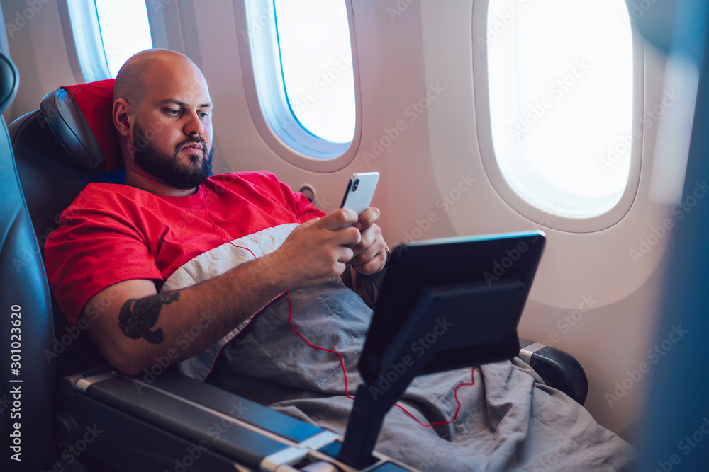 Poster caucasian male airplane passenger texting message on smartphone while connected to wireless internet