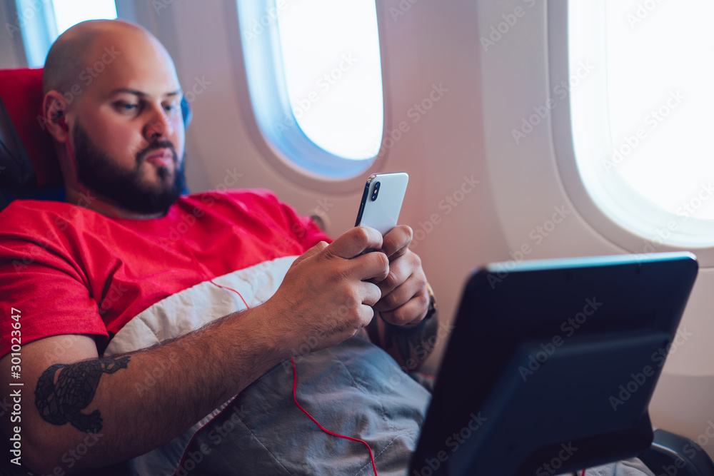 Poster caucasian male passenger relaxing in wide seat with large space and using wifi internet access on bo
