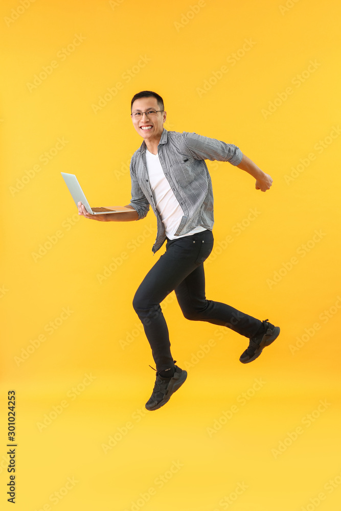 Poster happy jumping asian programmer with laptop on color background