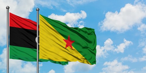 Libya and French Guiana flag waving in the wind against white cloudy blue sky together. Diplomacy concept, international relations.