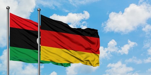 Libya and Germany flag waving in the wind against white cloudy blue sky together. Diplomacy...