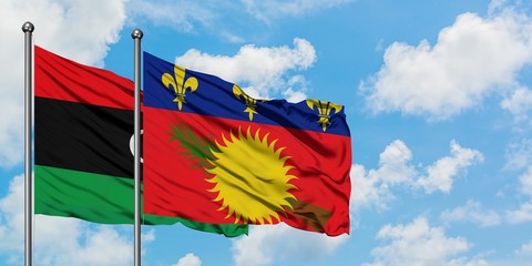 Libya and Guadeloupe flag waving in the wind against white cloudy blue sky together. Diplomacy...