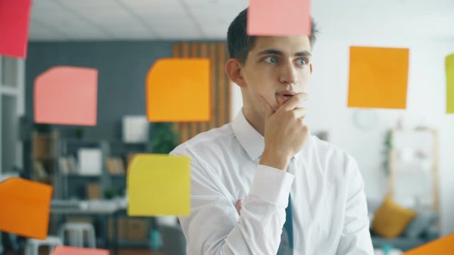Creative businessman brainstorming ideas working with sticky notes on glass in office. Close up 4k slow motion footage. Worker man in modern office.